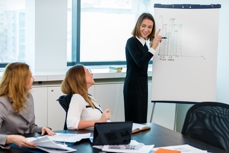 Serious girl standing with a marker near a whiteboard and drawing. Business, startup, planning, manager woman start writing on a flipchartの写真素材
