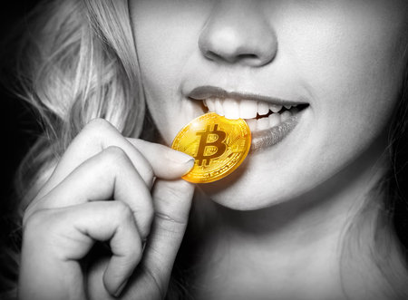 Sexy blonde girl checks bitcoin for authenticity with the help her teeth. Bitcoinの写真素材