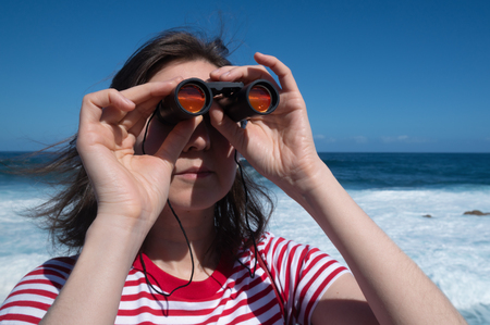 Girl tourist looking through binoculars on background of oceanの写真素材