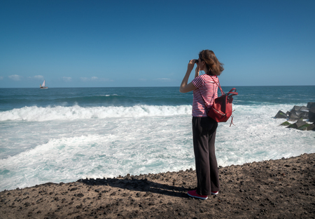 Girl looking through binoculars on the ocean and a yacht with a sailの写真素材