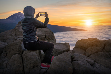Girl taking pictures on the phone of the sunset on the volcano Teide in Tenerifeの写真素材