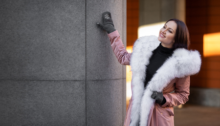 beautiful model on the street in the afternoon near the building. model on the street in a warm jacket with fur. cold weather outside. warm clothing with warm brown fur. beautiful model on the street during the dayの写真素材