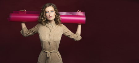 Girl model in the Studio with a roll of plastic on his shoulders. On a colored maroon backgroundの写真素材