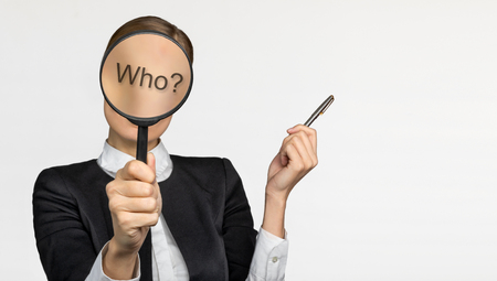 The girl in the office covered her face with a magnifying glass and we do not see her face. On the glass the writing Who. white background. The concept of employment and workの写真素材