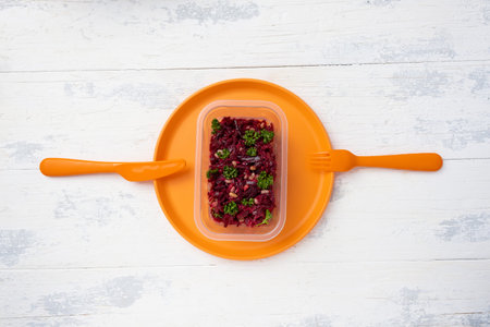 a portion of vinaigrette in a plastic box on a plastic orange plate with a plastic knife and fork on...