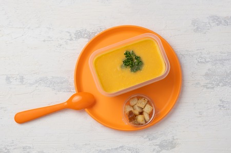 lentil vegetable soup in a plastic box on a plastic colored plate with a plastic spoon. on a white wooden tableの写真素材