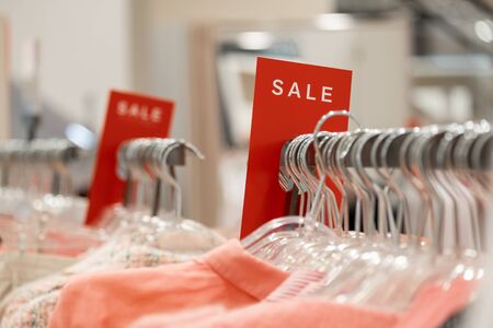 goods in stores and a red sign on sales discounts. mocap for text and concept of sales and trade in light industry. signs with the words sale in stores on hangersの写真素材