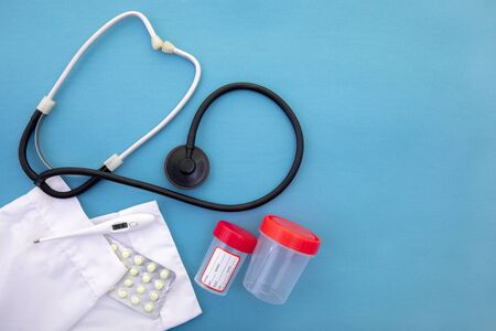 stethoscope next to a medical gown lying on a blue background next to a thermometer with containers for analysisの写真素材