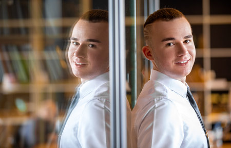 Portrait of a young male student in the office. a young man stands near the glass wall of the...