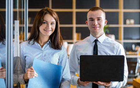 a young woman holding documents and a young man with a laptop in his hands working in the office of the company. portrait of young professionalsの写真素材