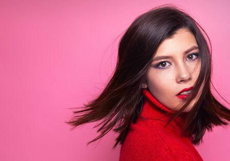 portrait of a girl at the time of turning the head. girl in a fleeting glance with hair in flight. feminine and cute portrait. girl in red sweater with collar. portrait of a girl in the Studioの写真素材