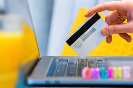 female hand with credit card and online payment using laptop. on the laptop in the blurring are colored lettersの写真素材