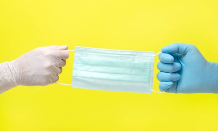 yellow background and hands in medical gloves.male and female hands in medical gloves pull on a medical mask. hands pulling a medical mask over themselves. competition for protection in medicineの写真素材