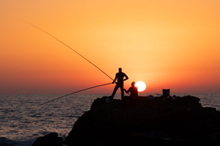 fishermen fishing in the evening by the sea on the Mediterranean sea coast of Caesarea in Israel at sunset time in the direction of the setting sun. High quality photoの写真素材