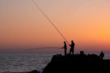 fishermen fishing in the evening by the sea on the Mediterranean sea coast of Caesarea in Israel at sunset time in the direction of the setting sun. High quality photoの写真素材