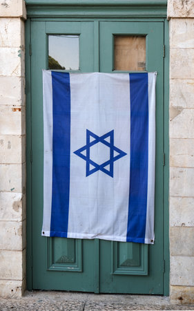 National flag of Israel with the Star of David displayed on a closed green door in an old stone building. Symbol of identity, culture, and patriotism in an urban settingの写真素材