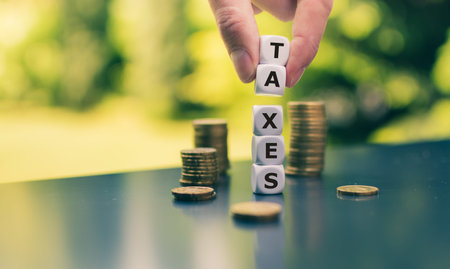 Dice form the word Taxes next to stacks of coins.