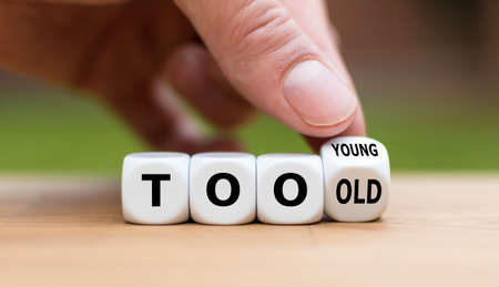 Hand turns a dice and changes the expression "too old" to "too young" , or vice versa.の写真素材