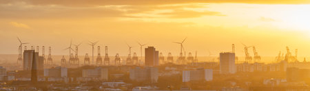 Cranes and wind turbines during sunset in the harbor area of Hamburg, Germany.