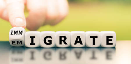 Hand turns a dice and changes the word "immigration" to "emigration", or vice versa.の写真素材