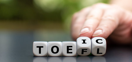 Hand turns dice and changes the acronym toefl to toeic, or vice versa.