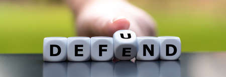 Hand turns dice and changes the word defend to defund.の素材 [FY310150315719]