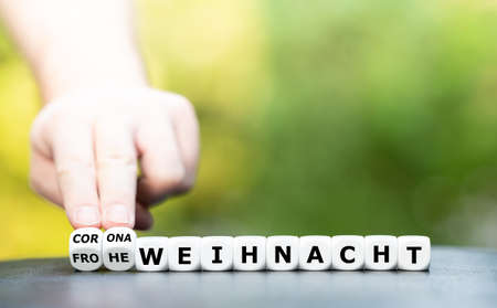 Symbol for a corona influenced Christmas. Hand turns dice and changes the German expression "Merry Christmas" to "Corona Christmas" (corona christmas).の写真素材