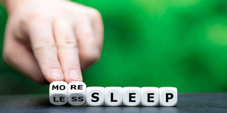 Hand turns dice and changes the expression "less sleep" to "more sleep".の写真素材