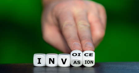 Symbol for the Russian invasion and the financial consequences. Hand turns dice and changes the word invasion to invoice.の写真素材