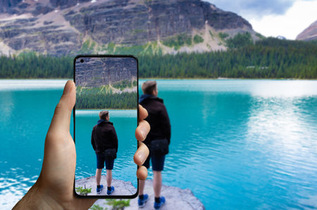 Tourist taking a picture with a mobile phone of a man standing at the lake Ohara, Canada.