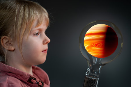 Young girl looks at a light bulb with a planet inside. Symbol for a curious child discovering the universe.の素材