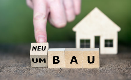 Hand turns wooden cube and changes the German expression 'Umbau' (rebuild) to 'Neubau' (new construction).の素材