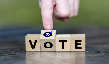 Hand turns wooden cube and puts a tick on the word vote. Symbol for participating in a voting process.の写真素材