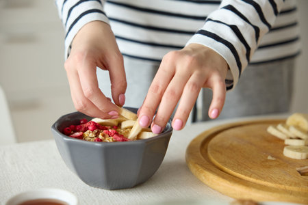 Cropped shot of unrecognizable woman with hands decorating putting bananas on bowl with strawberries...