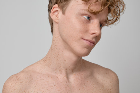 Beauty portrait of handsome freckled red haired and curly haired shirtless male with blue eyes clean skin fit body smiling and standing against gray background in studio shotの写真素材