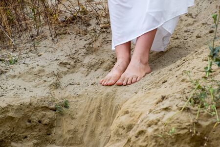 Legs of a girl in a white dress on the edge of a cliff. The sand is falling from the edge of the cliff.の写真素材
