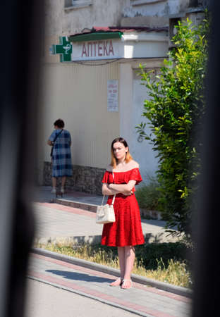 Balaklava, Republic of Crimea - June 9, 2019: A girl in a red dress waits for a bus on the side of the road.のeditorial素材