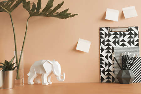 Pastel orange desk with leafs, elephant, plant, office accessories and sticky notes. Artist workspace.の写真素材