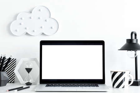 Modern and stylish desk with a cacti, cloud and laptop with white screen. Workplace of creative designer.の写真素材