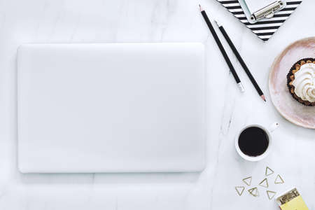 The top view of marble desk with cup of coffee, laptop, cake and notes. Concept for social media,...