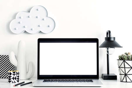 Modern and stylish desk with a cloud, office accessories, lamp, cacti and laptop mock up screen. Space of creative worker or freelancer.の写真素材