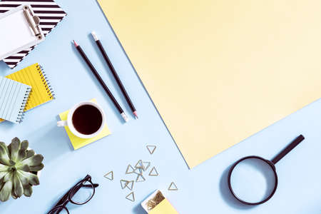 The top view of creative desk with school accessories, notebooks, glasses, memo and succulent. Blue and yellow background with copy space for inscription.の写真素材