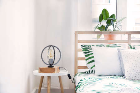 Modern and stylish bedroom with plants, design lamp and floral pattern bedding. Bright and sunny...
