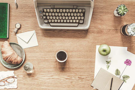 Stylish flat lay on wooden desk with typewriter, croissant, cup of coffee notebooks, succulents and...