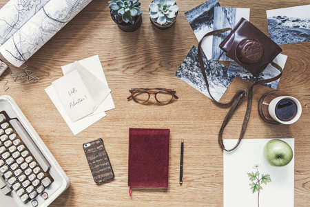 Modern composition of flat lay on wooden desk with typewiter, photos, notebook, retro camera , map and office accessories. Creative desk of traveler and adventure man.の写真素材