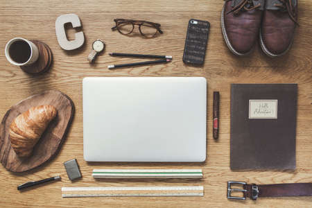 Modern composition of flat lay on wooden desk with laptop, phone, shoes notebook, glasses and office accessories. Creative desk of traveler.の写真素材