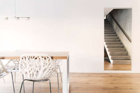 Stylish scandinavian dining room with wooden table, design chairs and lamp. Design space with white...