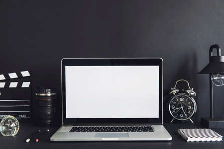 Stylish black desk with laptop mock up screen, black accessories and plant. Black backgrounds wall....