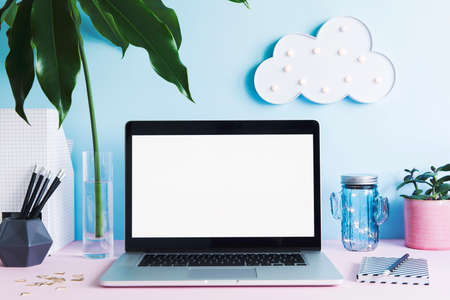 Stylish and creative desk with laptop mock up screen, office accessories, tropical leaf, cup and...