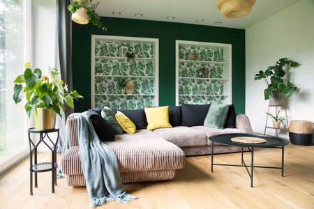 Stylish interior with sofa, colors pillows, flowers and wooden floor. Sunny and bright living room...